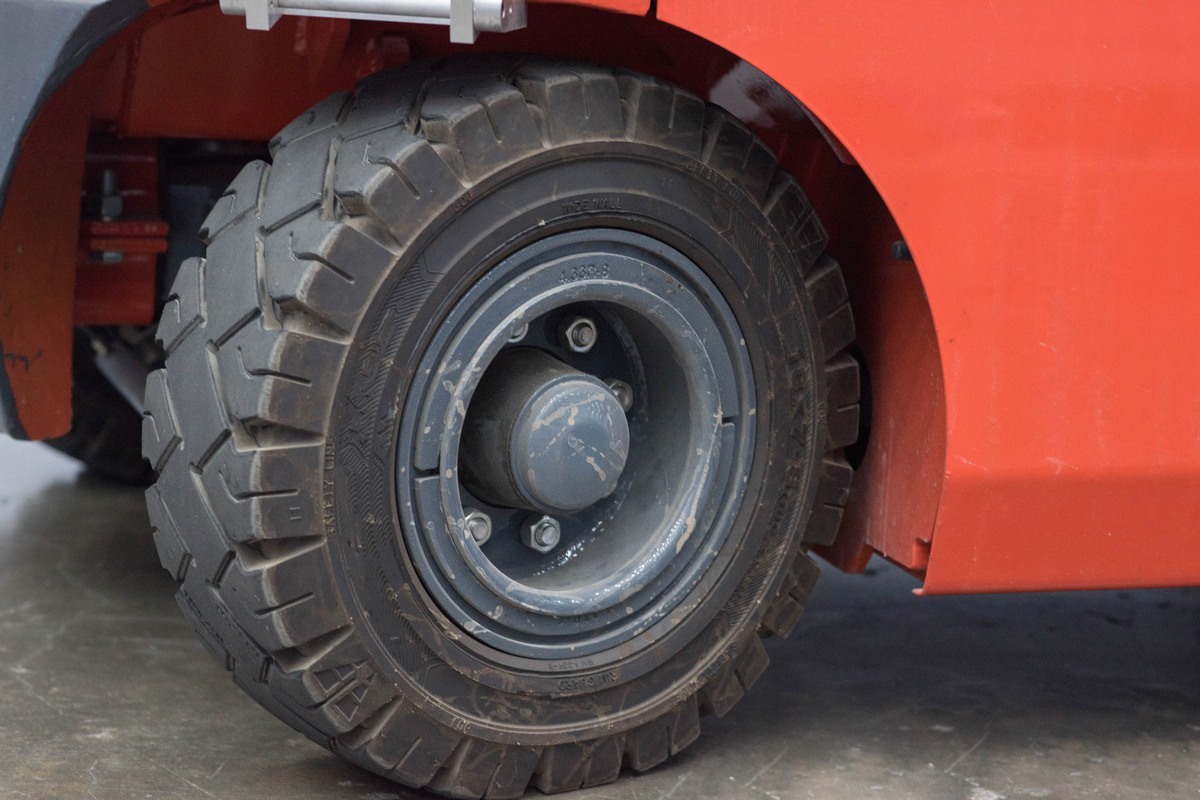 Close-up of a black lug-tread tire on a grey steel wheel under the red fender of a forklift, with molded lettering on the sidewall