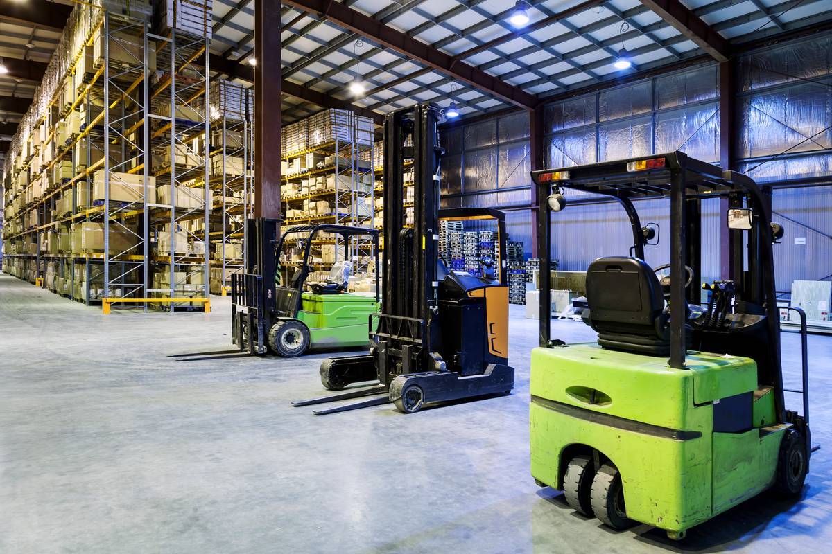 Green three-wheel electric forklift and a reach truck parked on smooth concrete in a racked warehouse
